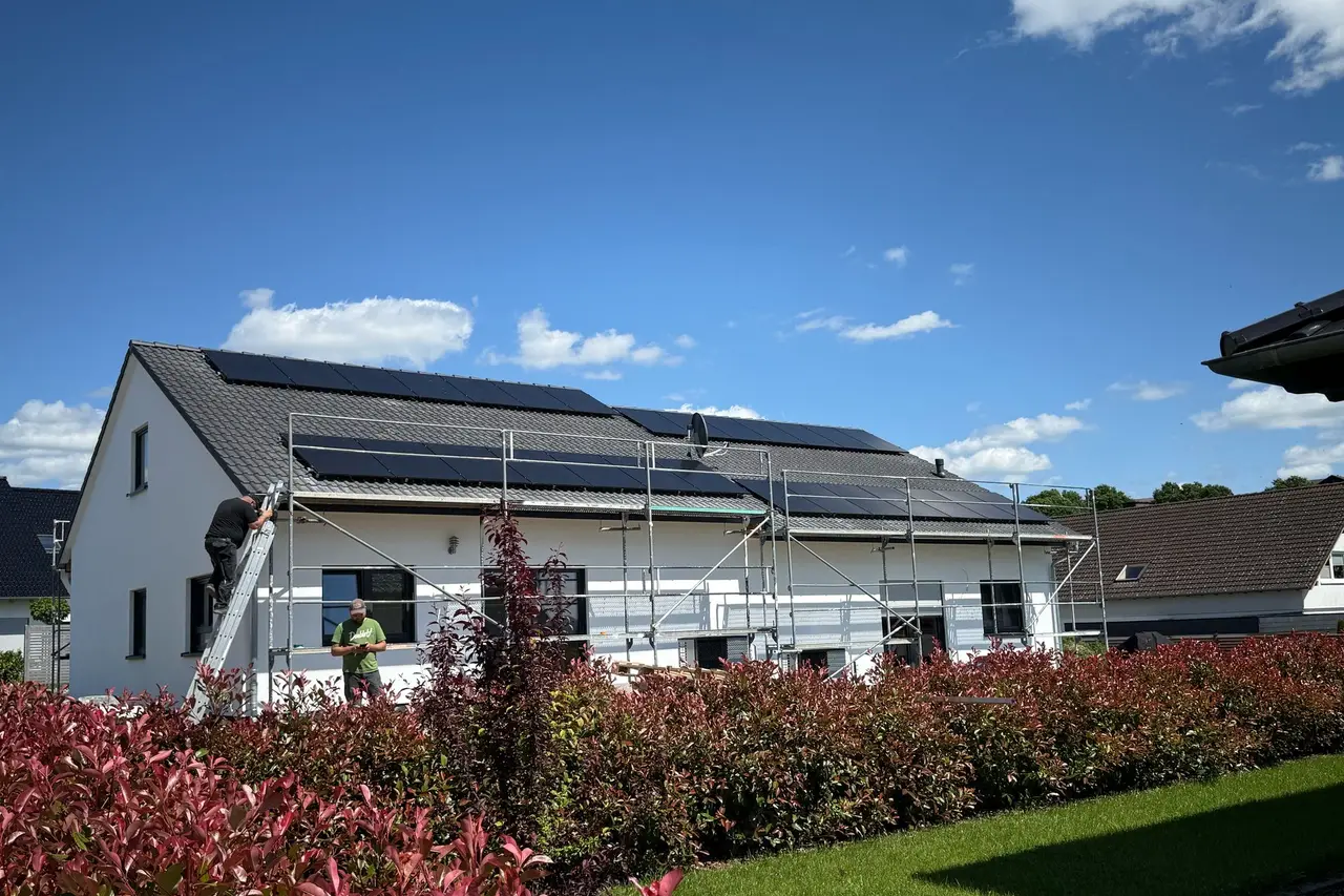 Einfamilienhaus mit Gerüst, zwei Monteure setzen Solarmodule auf das Dach