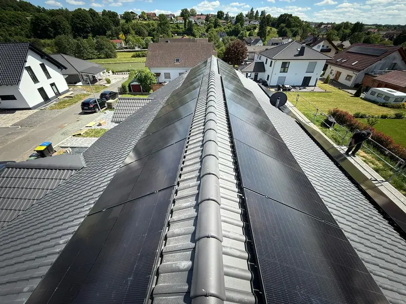 Luftaufnahme eines Dachfirsts mit Solarmodulen über einer Wohnsiedlung