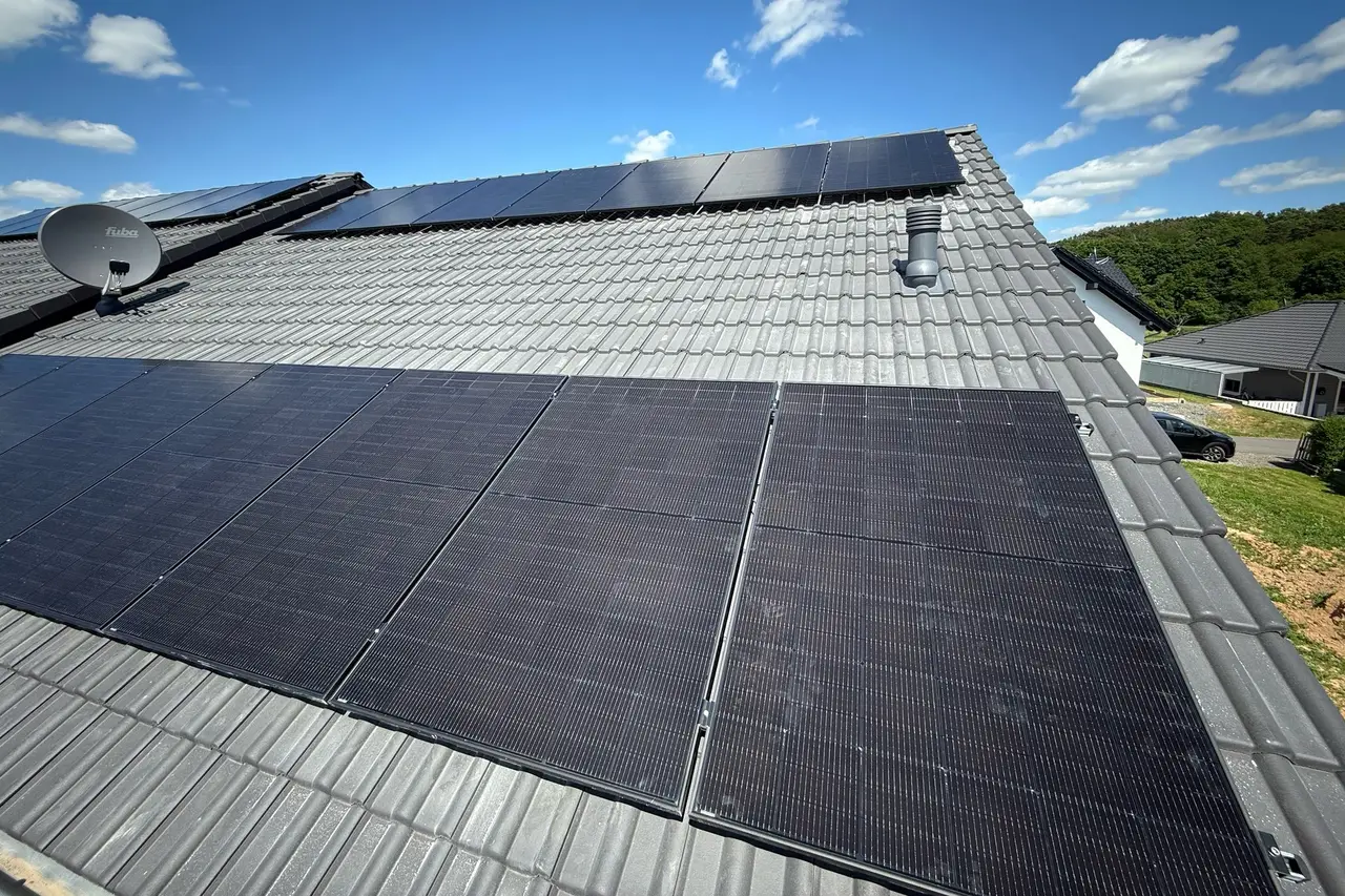 Fertig montierte Solarmodule auf einem grauen Ziegeldach unter blauem Himmel