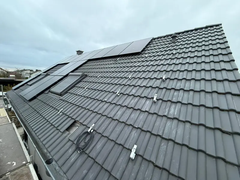 Ziegeldach mit Montagehaken und ersten Modulen neben einem Dachfenster
